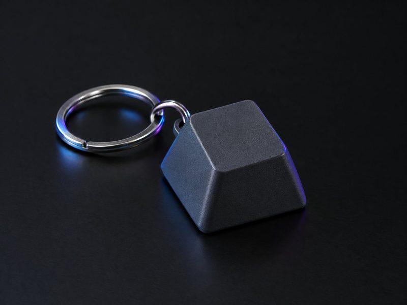 Concept render: Keycap keyring. An oversized keyboard keycap on a ring, the name on top.