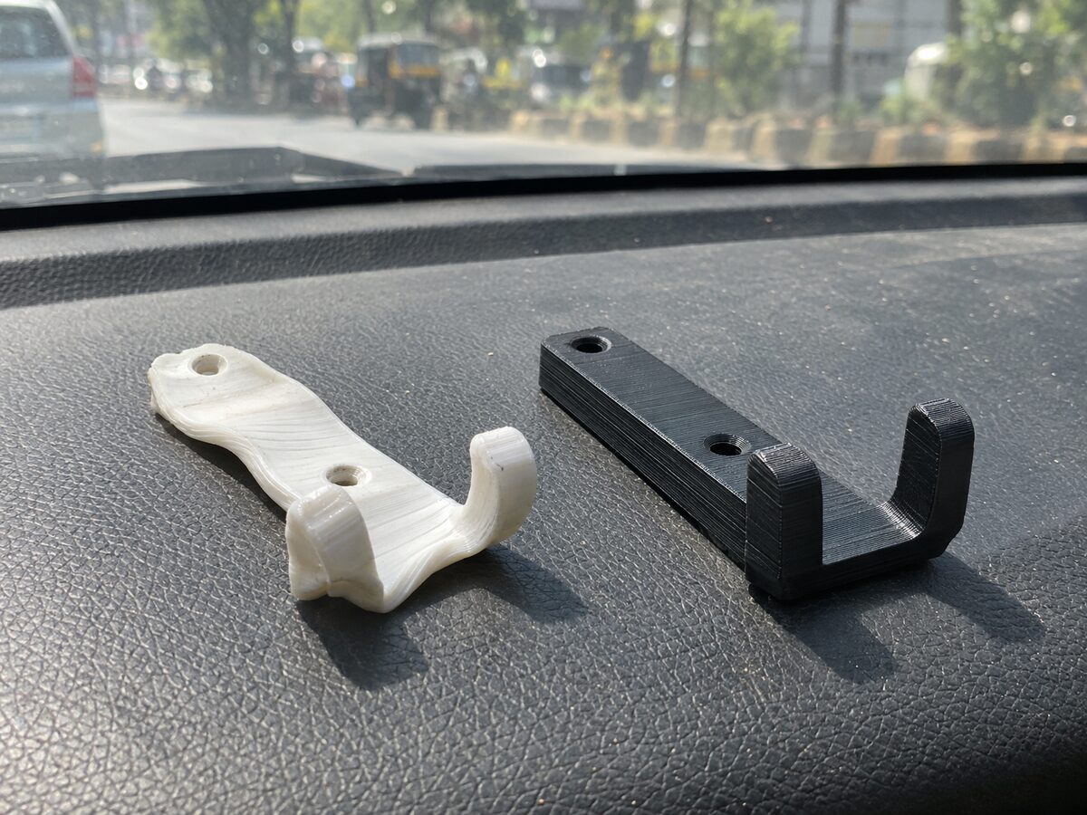 Two identical printed phone-mount brackets on a sun-baked car dashboard: the white PLA one sagged and warped by heat, the black ASA one still straight