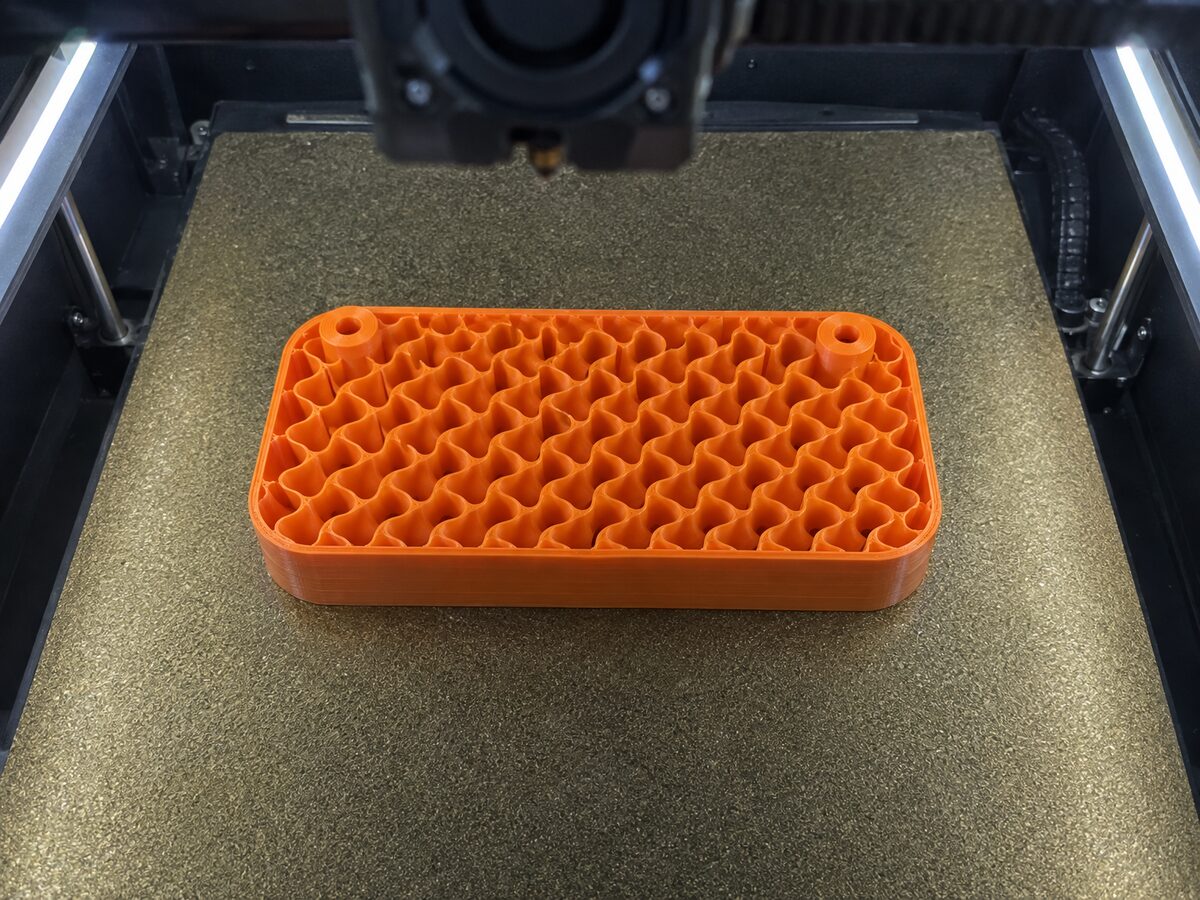 Orange 3D print stopped halfway inside an enclosed FDM printer, its open top showing a wavy gyroid infill lattice inside solid outer walls