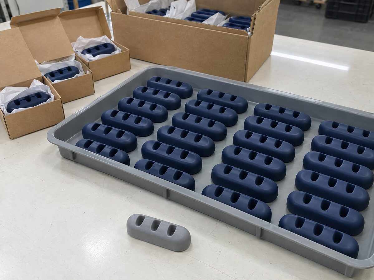Tray of identical navy cast cable organisers with their grey resin master in front, and boxed units on a packing table