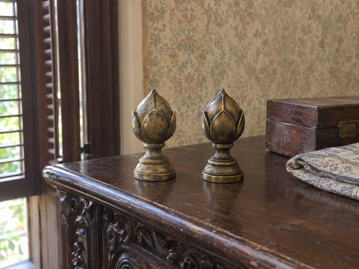 An original tarnished brass lotus-bud finial and a printed replacement painted to match, side by side on a carved rosewood cabinet in an old bungalow